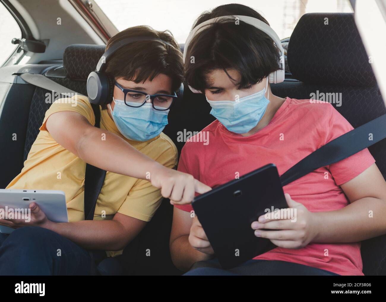 due bambini con maschera medica a cavallo in un'auto da gioco con un tablet Foto Stock