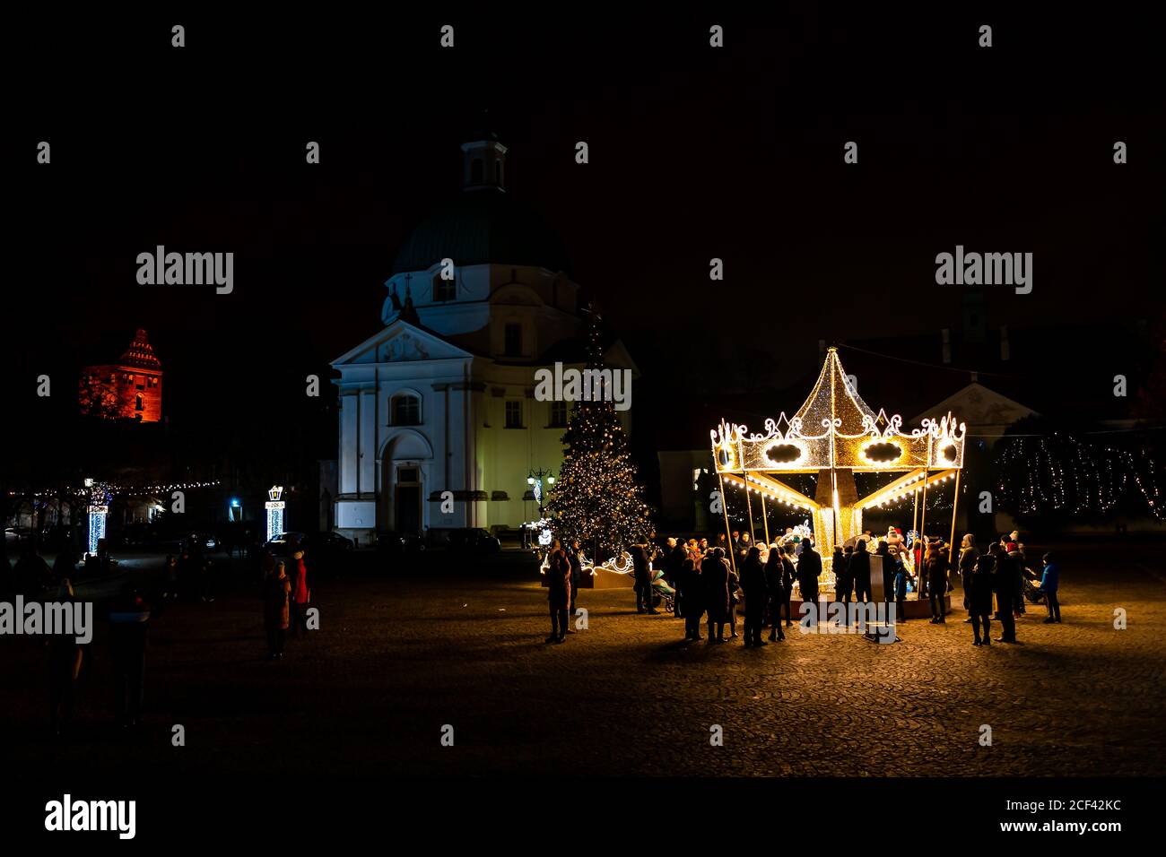 Varsavia, Polonia - 26 dicembre 2019: Piazza del mercato di New Town rynek con la famosa chiesa e giostra di notte con molte persone illuminate luci Foto Stock