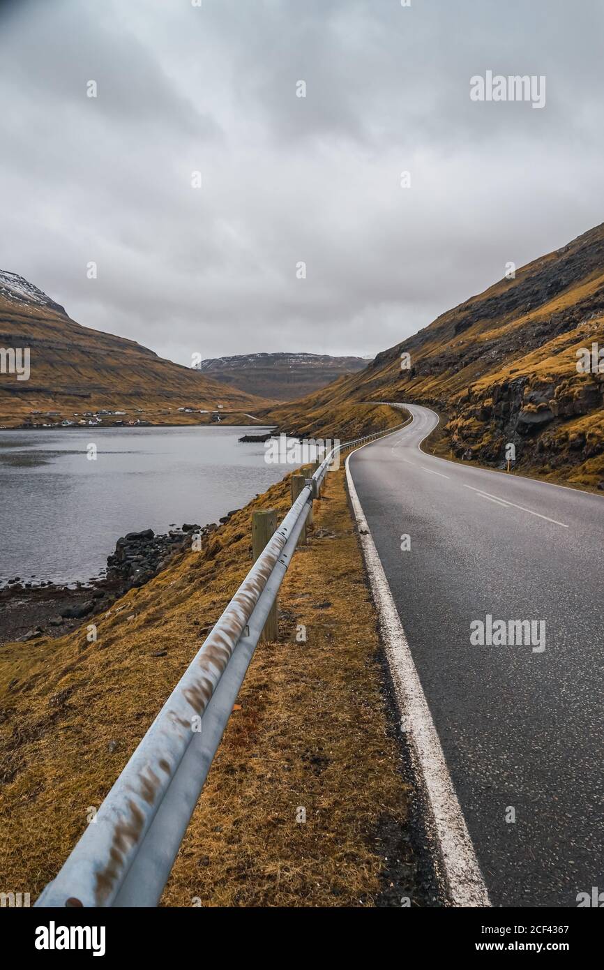 Strada asfaltata curvilinea che attraversa terreni collinosi in giornata nuvolosa Sulle Isole Faroe Foto Stock