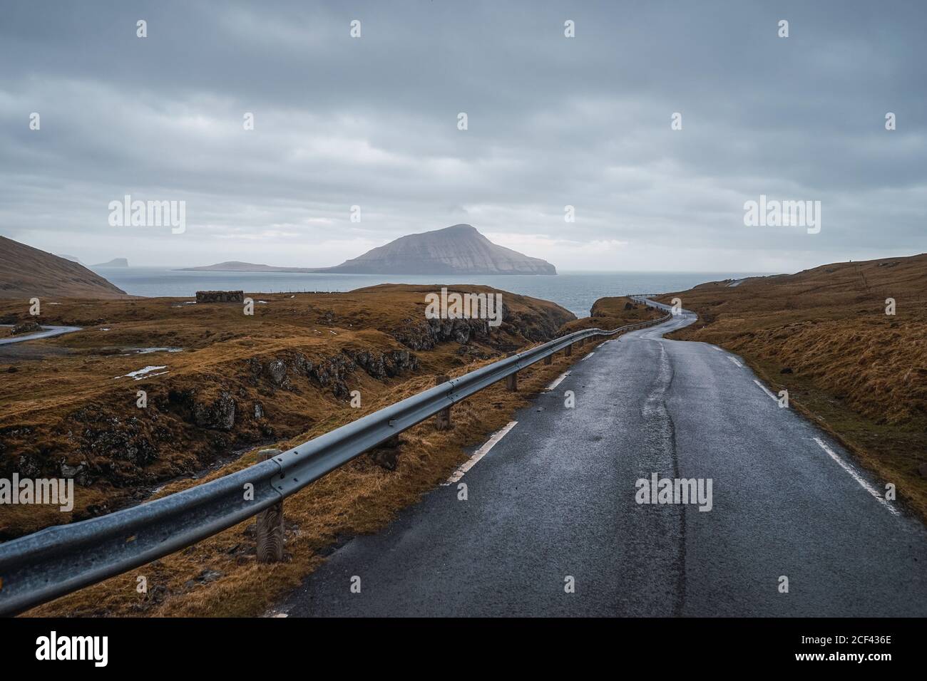Strada asfaltata curvilinea che attraversa terreni collinosi in giornata nuvolosa Sulle Isole Faroe Foto Stock