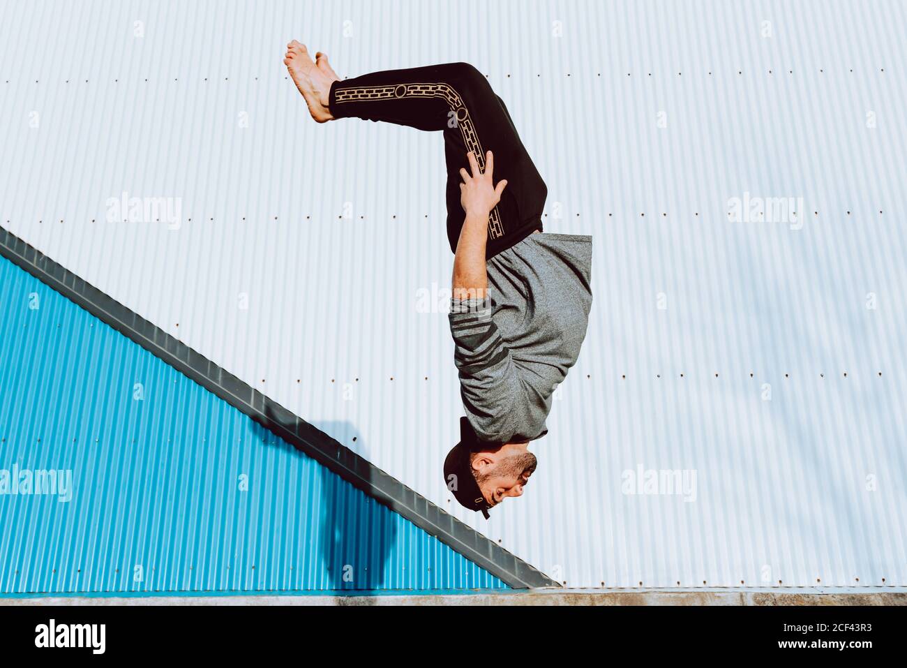 Vista laterale del ragazzo a piedi nudi in un elegante vestito che esegue il flip vicino al muro di un edificio moderno sulla strada della città Foto Stock
