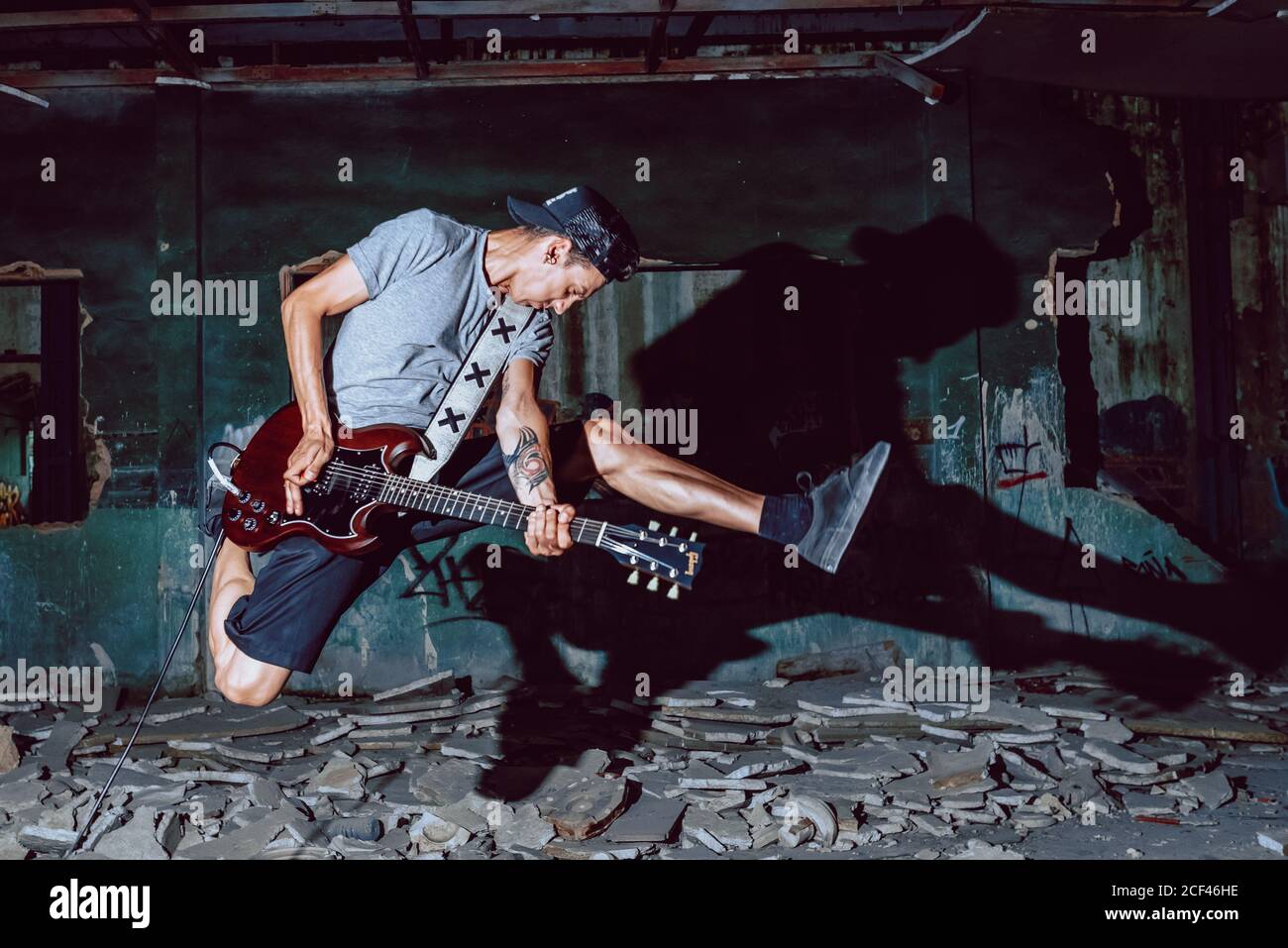 Il musicista maschile salta in modo espressivo mentre suona la chitarra elettrica al buio sala in rovina grugnosa Foto Stock
