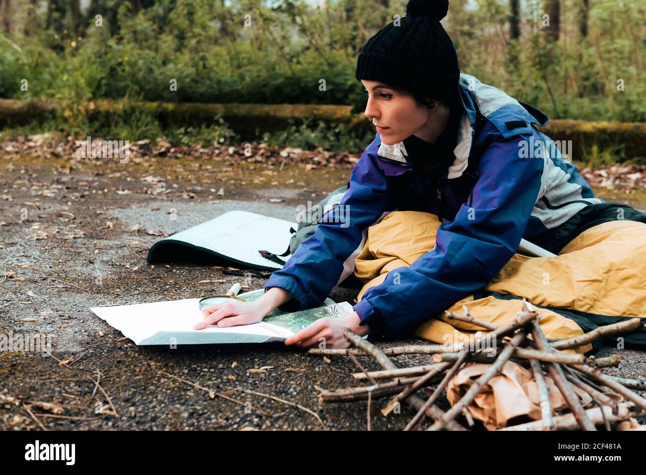 Concentrato giovane donna zaino in spalla ricerca posizione sulla mappa mentre si siede a terra durante il trekking nella foresta in autunno giorno Foto Stock