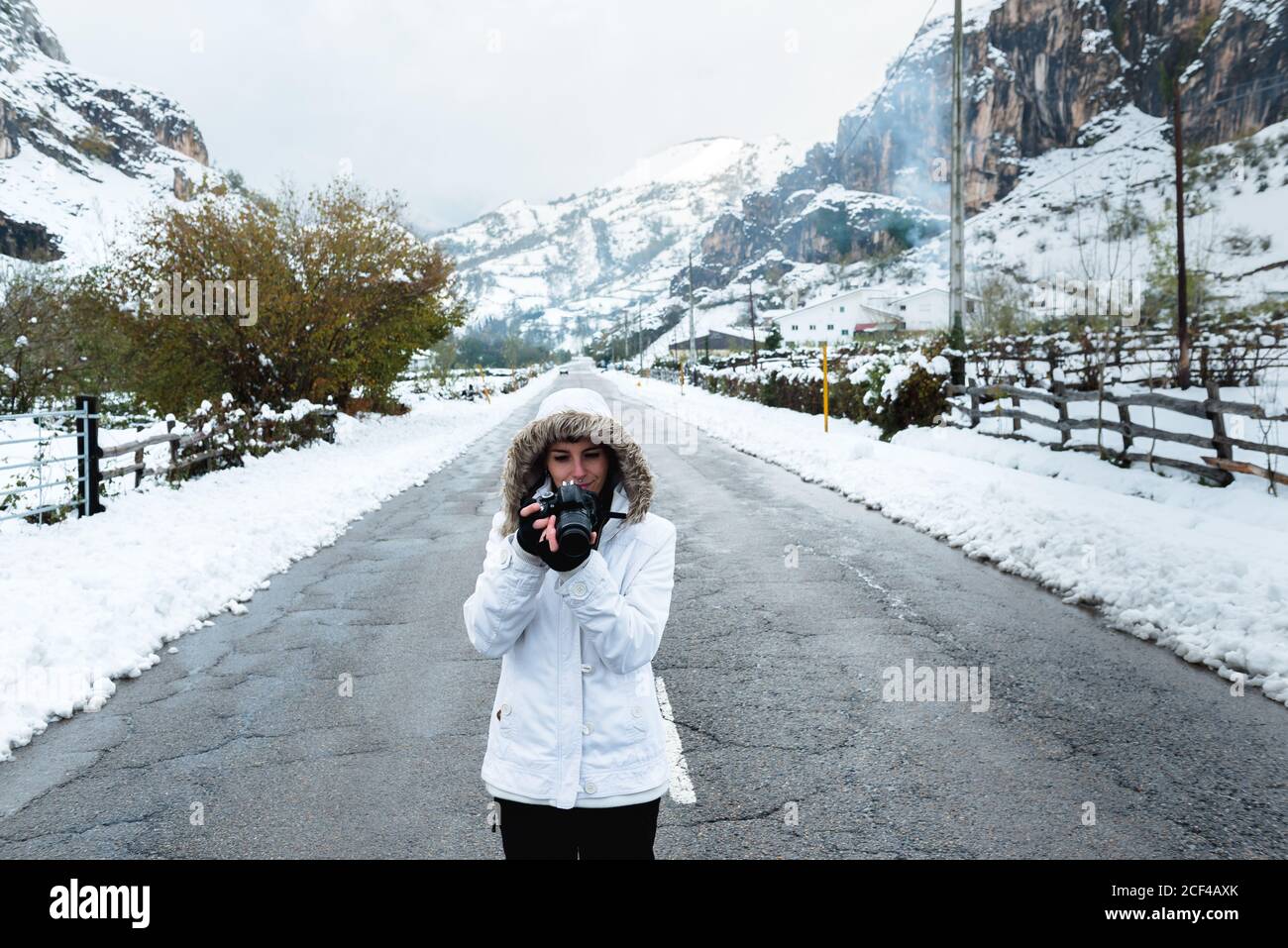 Donna focalizzata in giacca invernale bianca con cappuccio e nero pantaloni  che scattano foto con la