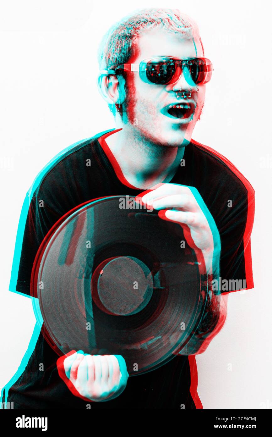 Giovane felice hipster maschio bello in occhiali da sole eleganti che tengono il vinile registra in stile grafico tridimensionale Foto Stock