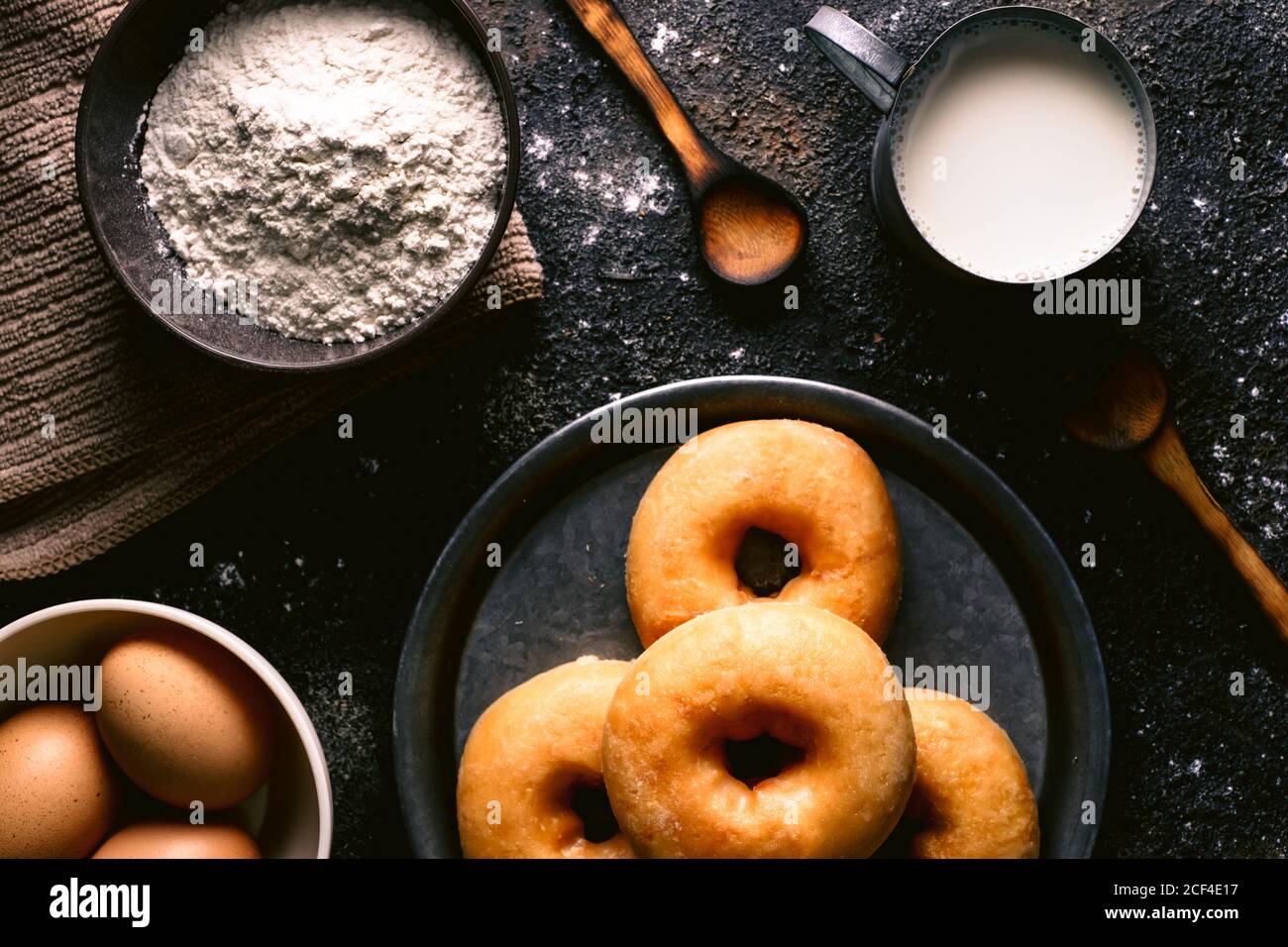 Vista dall'alto delle ciambelle fresche poste sul tavolo vicino vari ingredienti di pasticceria e utensili in cucina Foto Stock