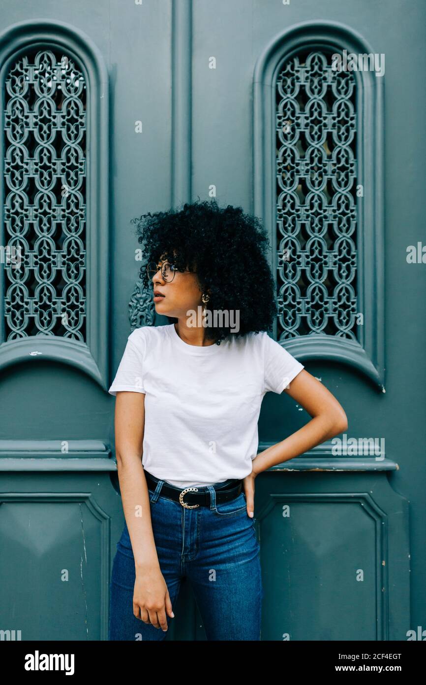 Bella donna etnica in t-shirt bianca e jeans appoggiati su porta verde e gli occhi chiusi Foto Stock