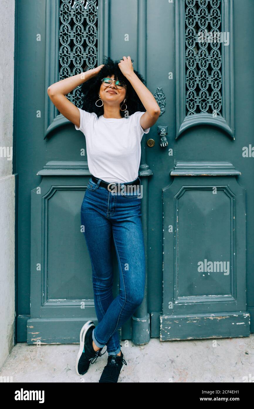 Bella donna etnica in t-shirt bianca e jeans appoggiati su porta verde e gli occhi chiusi Foto Stock