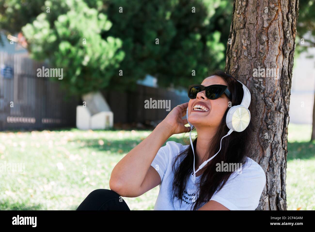Donna pacifica in occhiali da sole e cuffie ascoltare musica mentre si  siede sull'erba nel parco Foto stock - Alamy