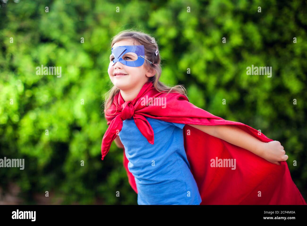 Supereroe ragazzina contro sfondo verde all'aperto. Infanzia, successo e concetto di potere Foto Stock