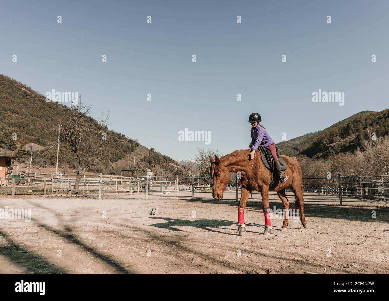 Giovane femmina in casco equitazione meraviglioso in recinto contro cielo blu senza nuvole durante la lezione sul ranch Foto Stock