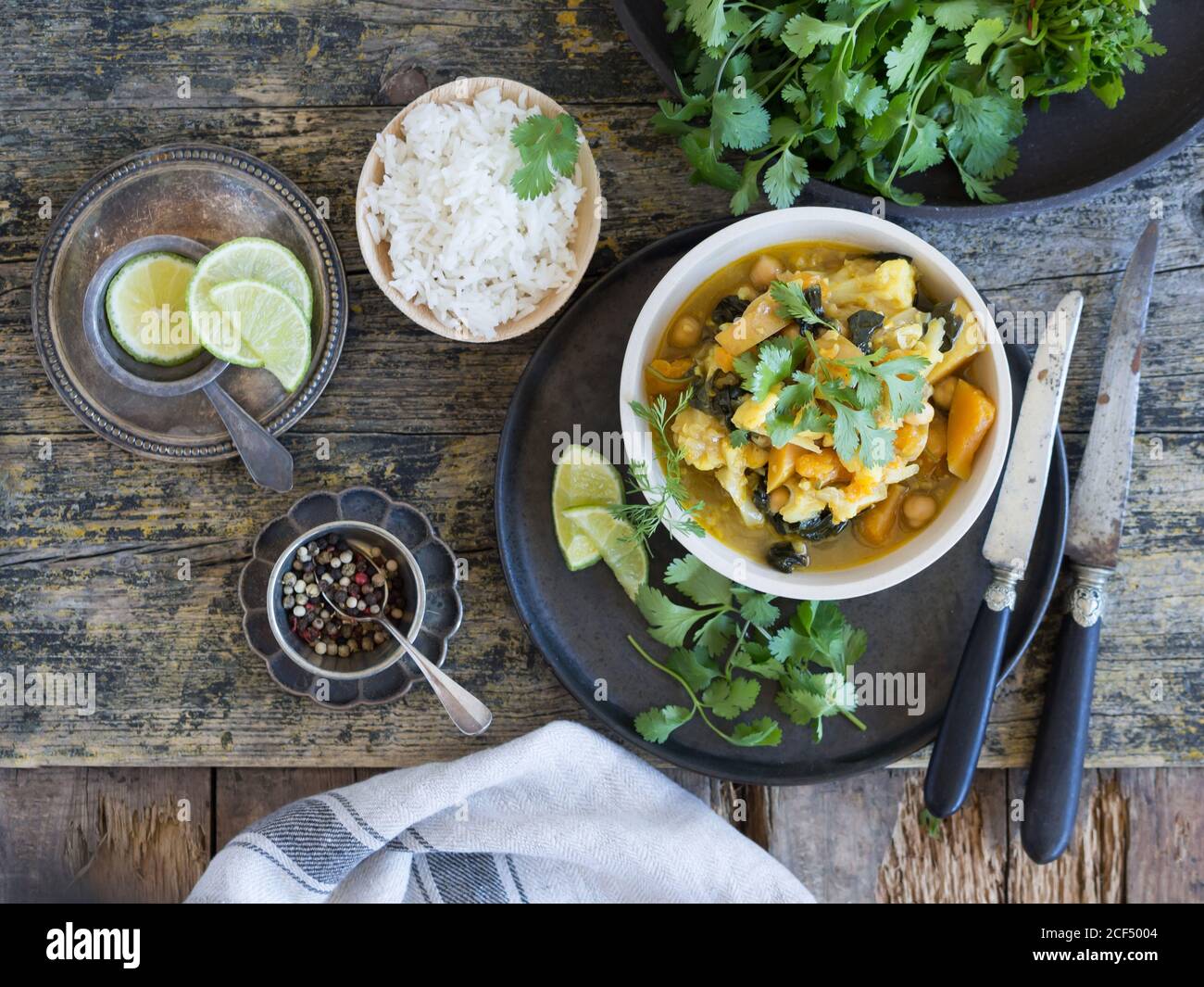 Da sopra piatto con deliziosi curry vegetariano e fette di lime posto su vassoio su sfondo di legno accanto alle piastre con pepe di riso e lime fresche Foto Stock