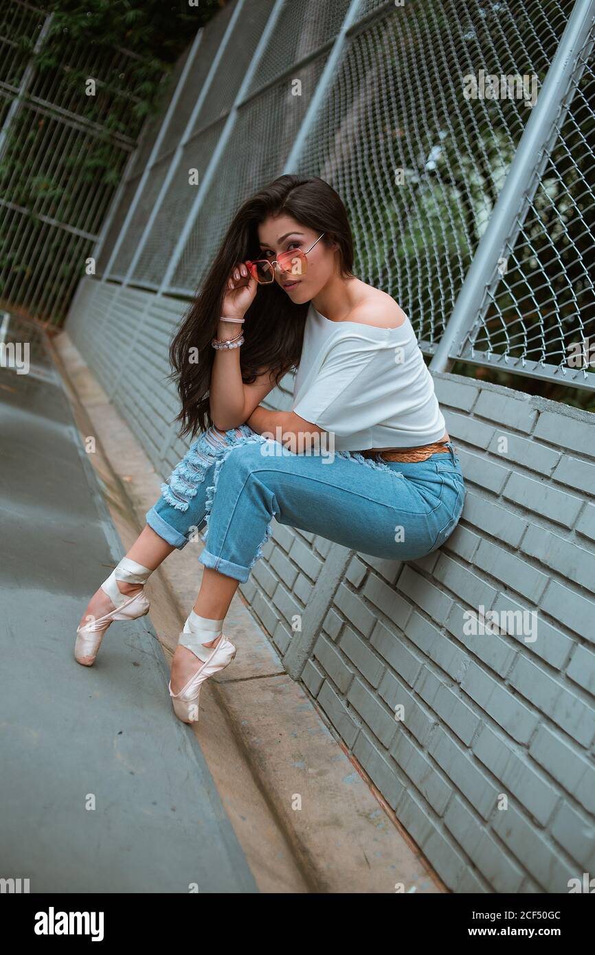 Vista laterale della ballerina donna sottile in abiti casual e. occhiali da  sole appoggiati sulla punta con scarpe appuntite su mattoni recinzione a  muro sulla strada Foto stock - Alamy