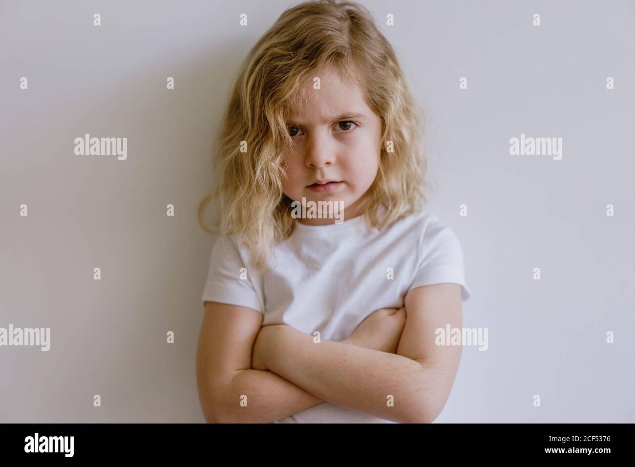 Deluso bambino piccolo in t-shirt casual guardando la macchina fotografica su sfondo bianco in studio Foto Stock