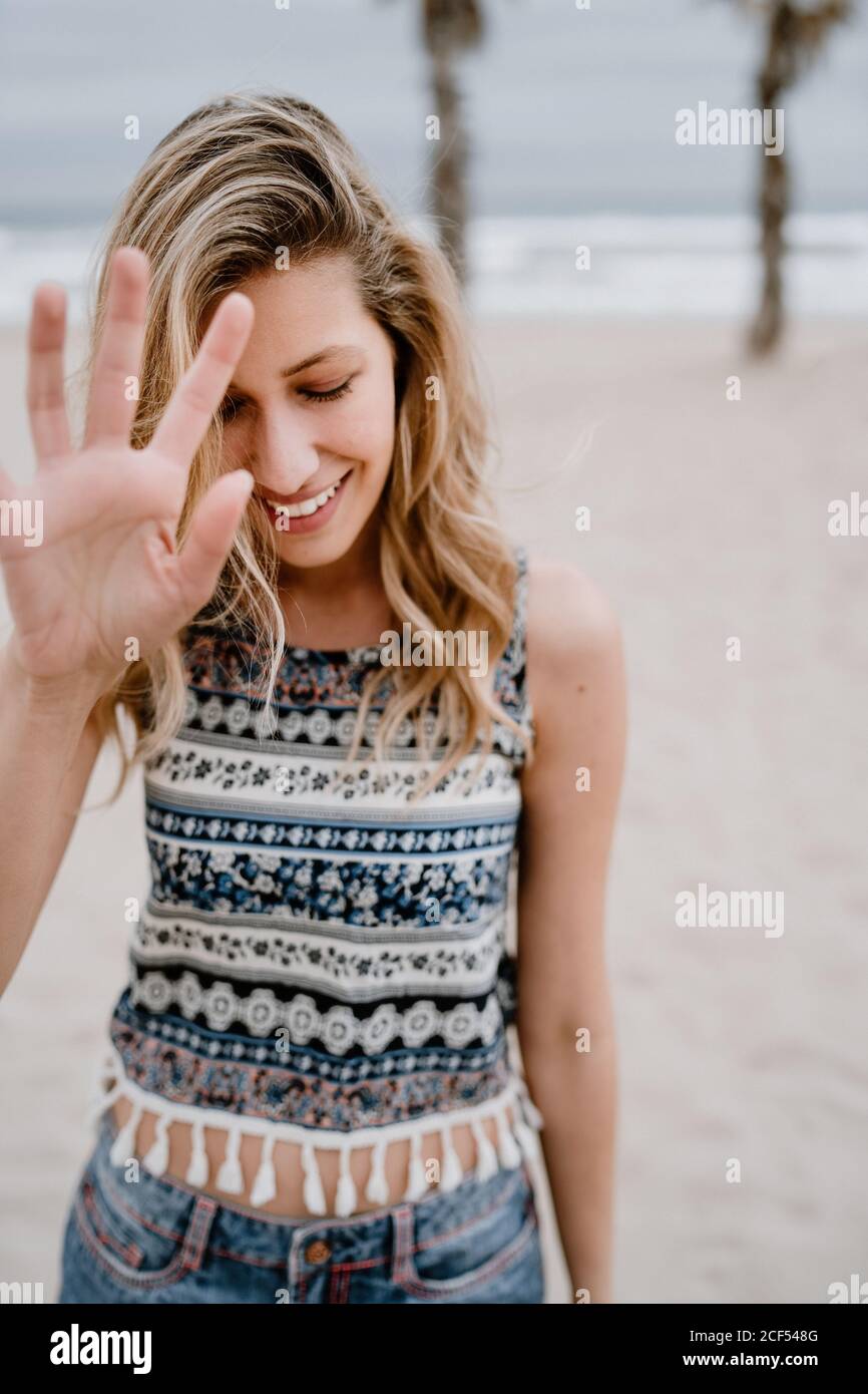 Allegro bionda Donna in top colorato e jean Shorts bloccare il suo viso con mano sulla riva del mare Foto Stock