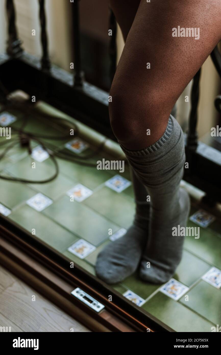 Dall'alto del raccolto femmina etnico irriconoscibile in ginocchio accogliente calzini in piedi sul balcone mentre riposano a casa Foto Stock