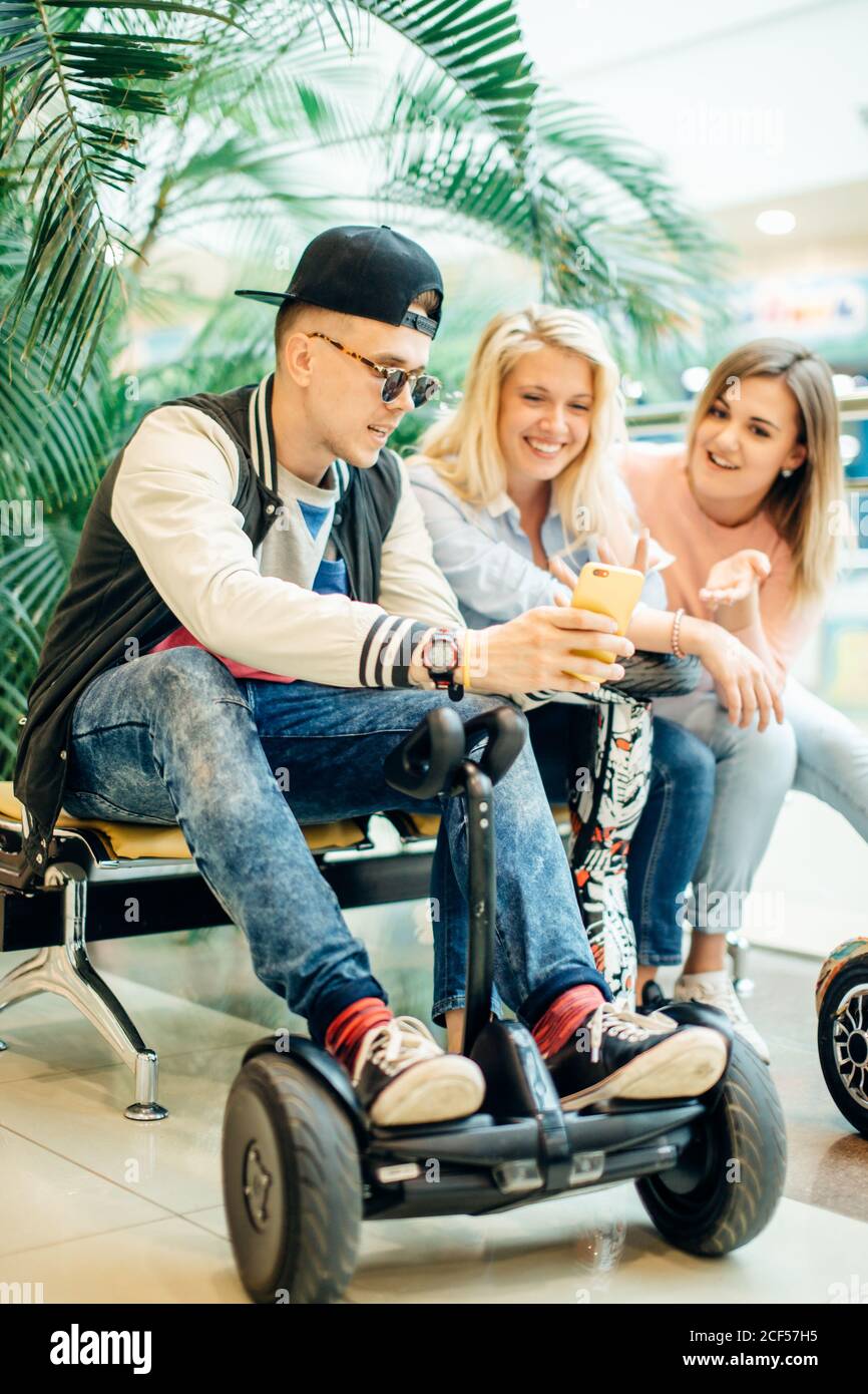 Gruppo di gente moderna con lo scooter elettrico hoverboard seduto al banco di lavoro e utilizzando il telefono Foto Stock