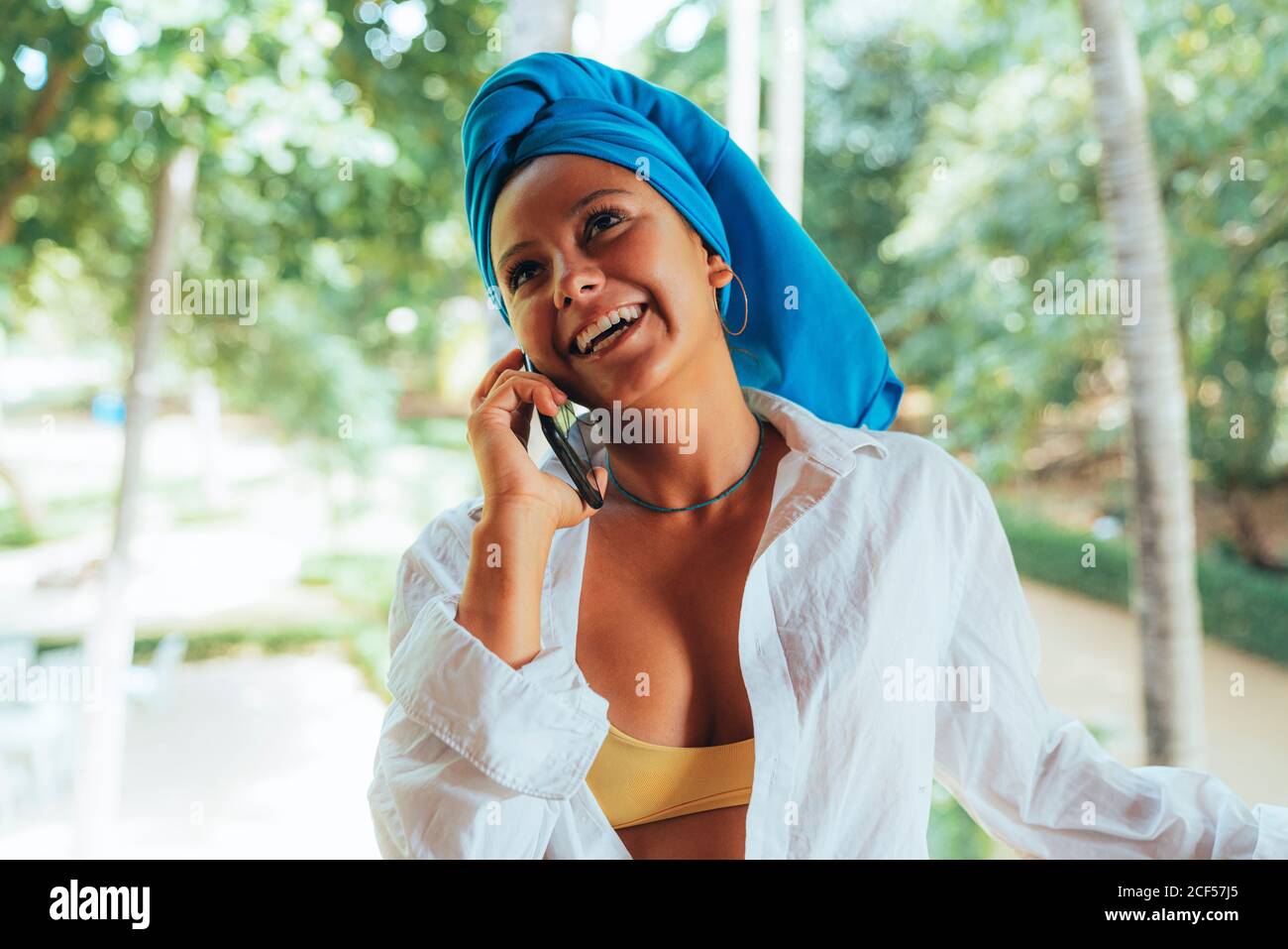 Donna allegra con capo wrap sorridente parlando su smartphone mentre si è in piedi in parco in Costa Rica Foto Stock