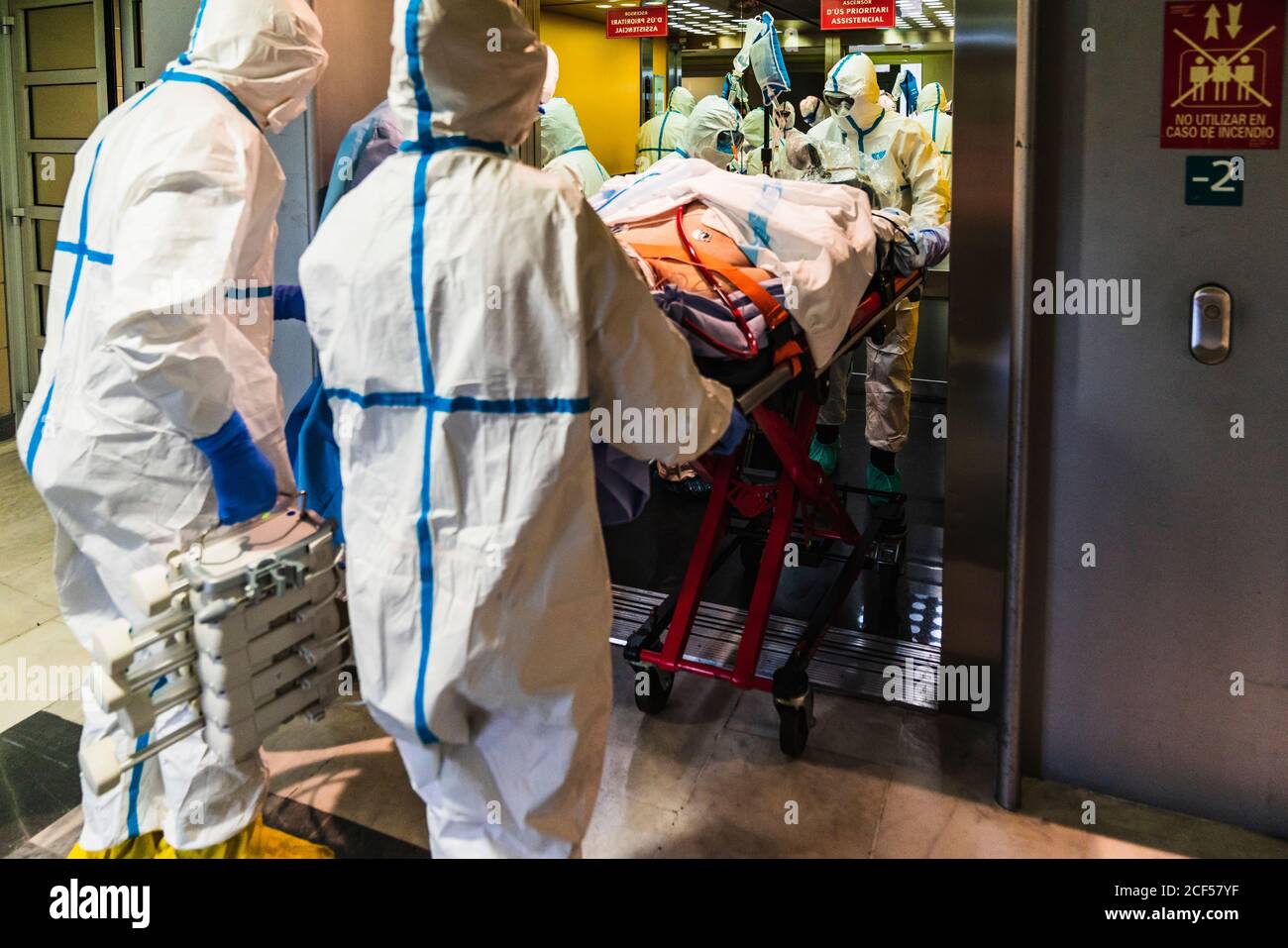 Gruppo di medici irriconoscibili che indossano l'uniforme protettiva mentre prendono il paziente con virus da ascensore in ospedale Foto Stock