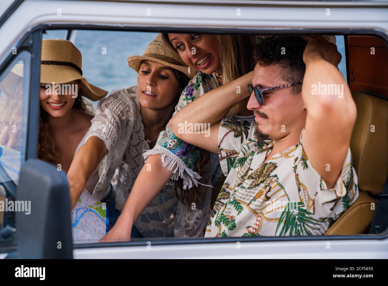 Vivaci donne allegre in cappello che punta sulla strada nella mappa mentre l'uomo cerca di scegliere il modo giusto in auto dentro giorno luminoso Foto Stock