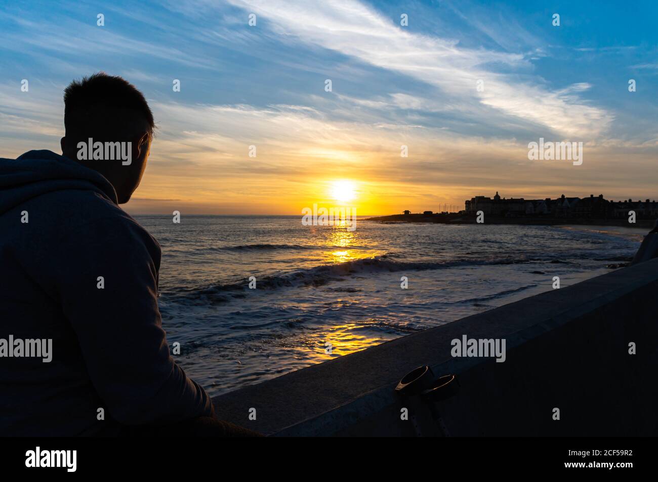 Giovane maschio sedette sulla parete guardando il tramonto a porthcawl galles uk, concentrarsi su sfondo maschile, blured Foto Stock