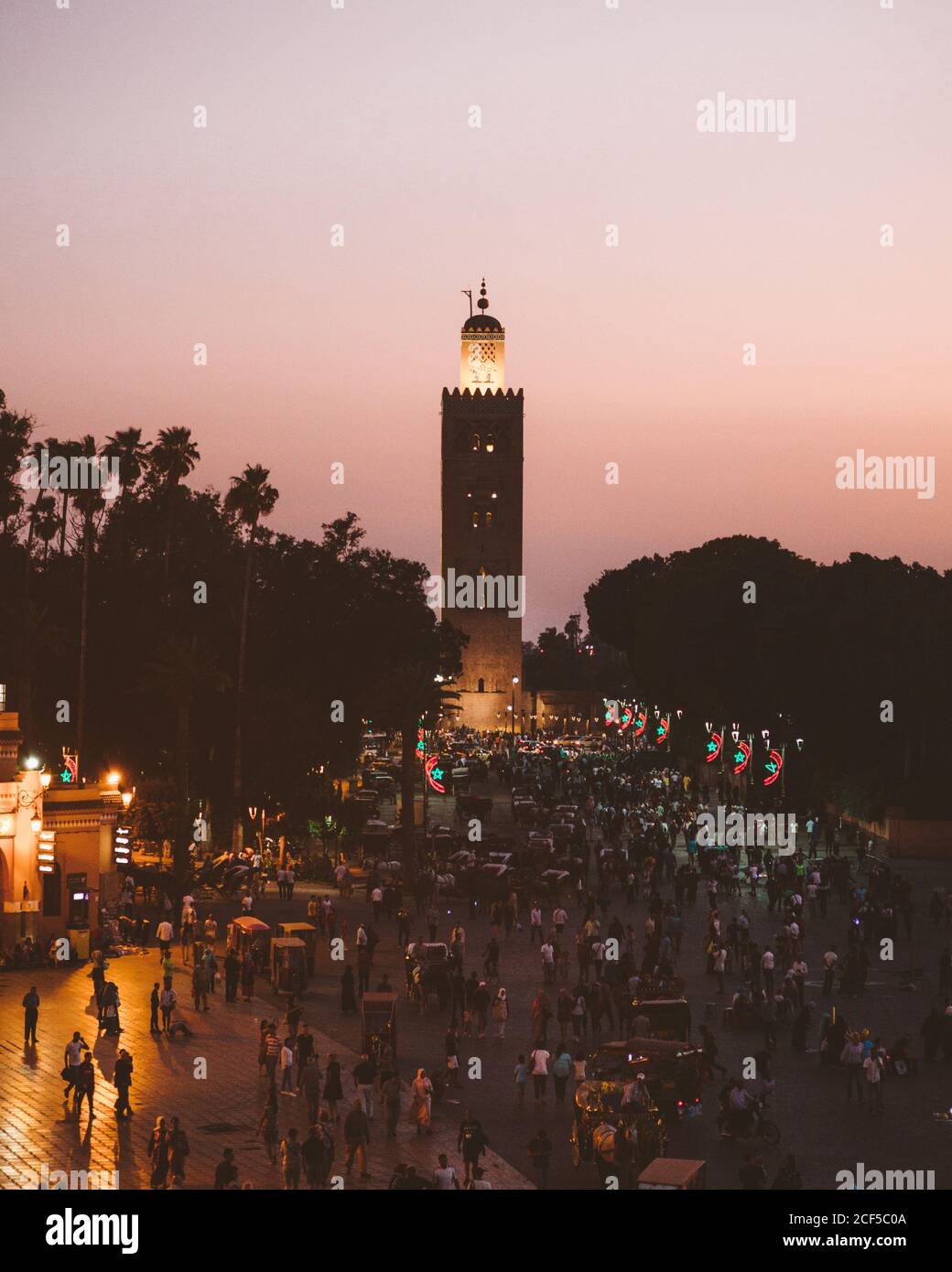 Marocco - Aprile 08 2019: Folla di persone anonime che camminano sulla piazza di fronte alla torre alta invecchiata durante il tramonto Foto Stock