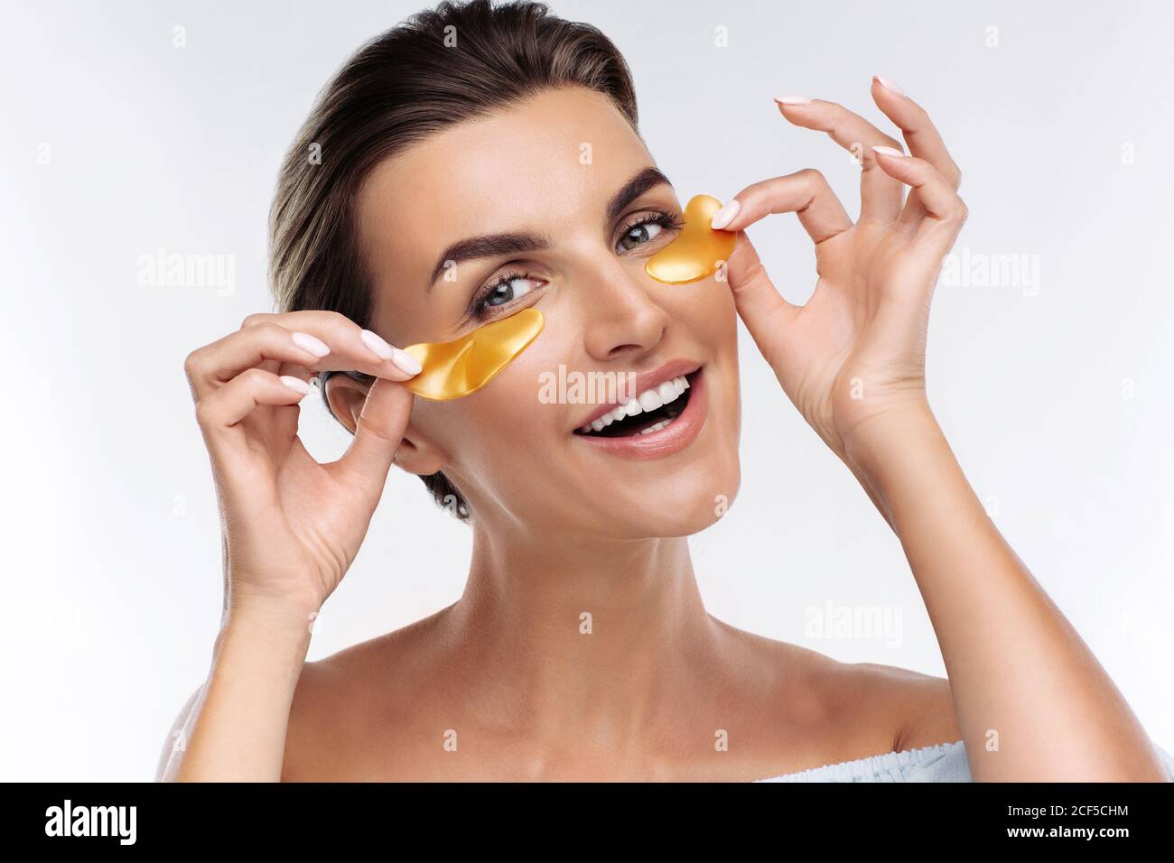Donna felice che applica le macchie dorate di idrogel ialuronico sotto gli occhi, isolato su sfondo bianco. Cura della pelle, trattamento di bellezza per ridurre la puffiness Foto Stock