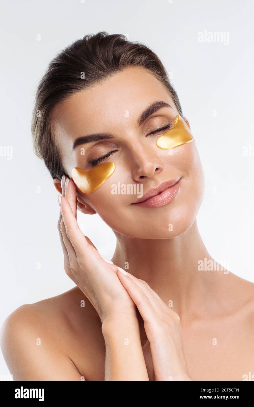 Closeup ritratto di donna di bellezza con make-up naturale applicando Golden Hydrogel cerotti sotto gli occhi. Giovane donna adulta con pelle pulita e fresca Foto Stock