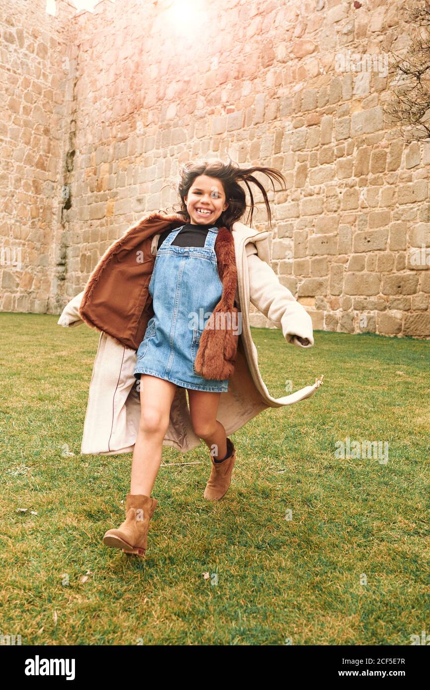 Allegra ragazza adolescente felice che corre con le braccia aperte in un prato verde in un parco guardando la macchina fotografica Foto Stock