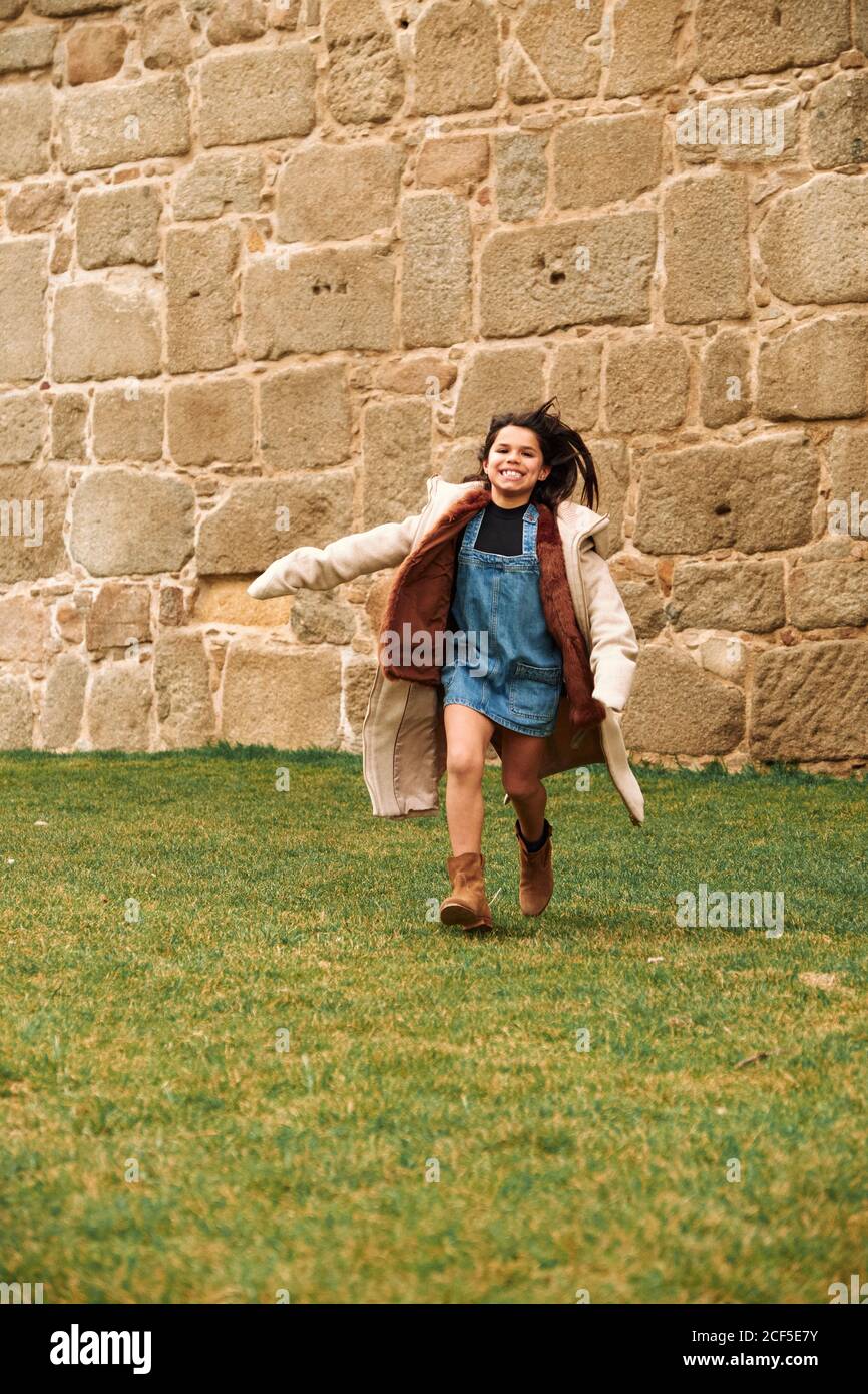 Allegra ragazza adolescente felice che corre con le braccia aperte in un prato verde in un parco che guarda lontano Foto Stock
