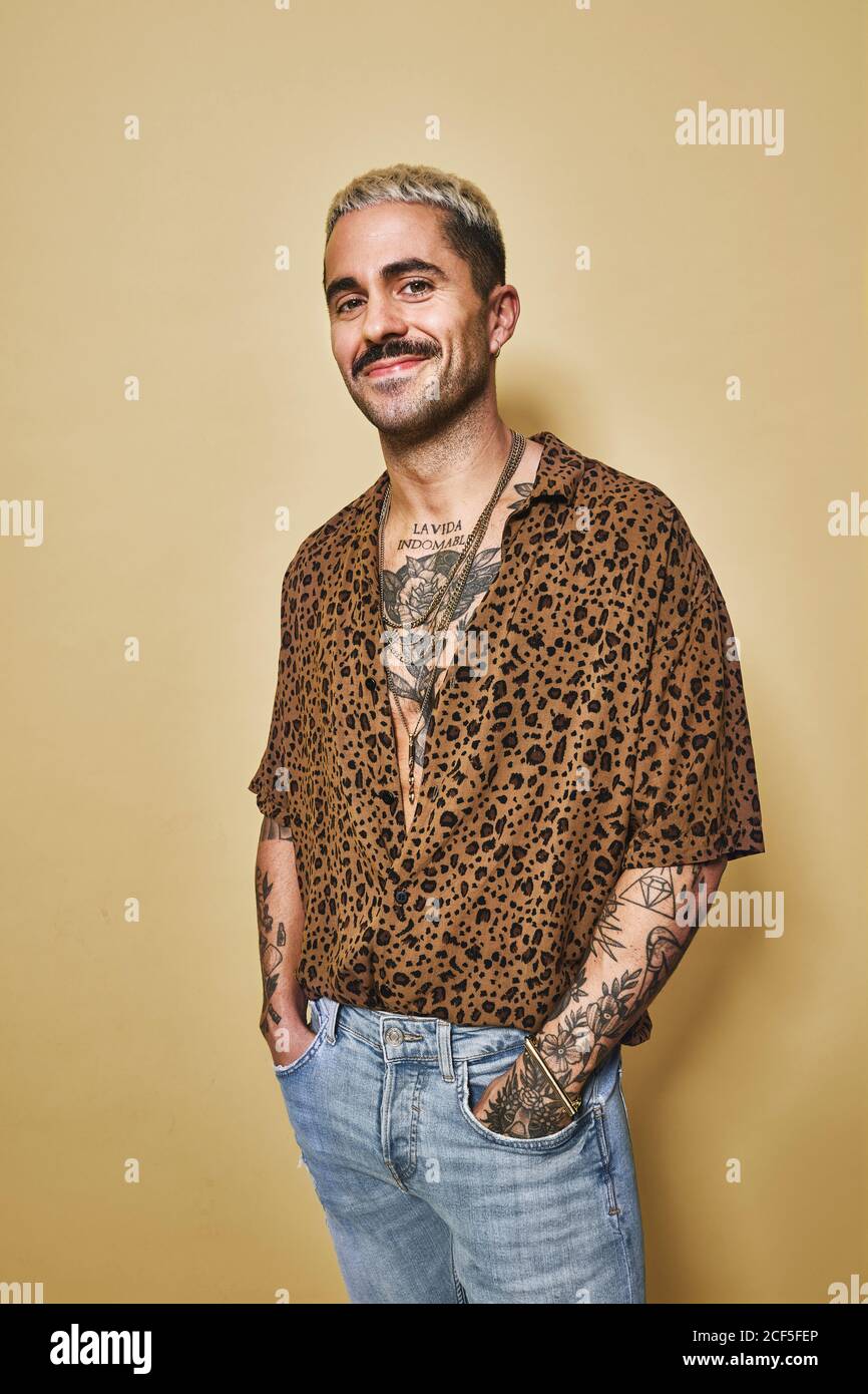 Modello maschile alla moda con tatuaggi che indossano una camicia leopardata  alla moda e. jeans in piedi su sfondo beige e guardando la macchina  fotografica Foto stock - Alamy