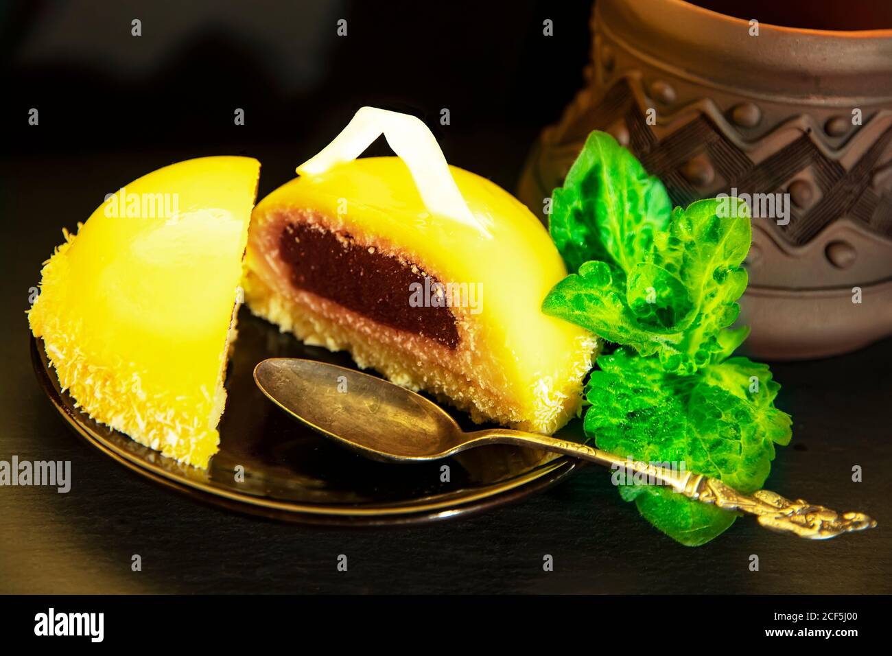 Deliziosi biscotti mousse con ripieno di bacche su un piatto scuro, un cucchiaio d'argento, petali di menta e una tazza di argilla ceramica con caffè su un tavolo in un caffè. Gastronomia Foto Stock