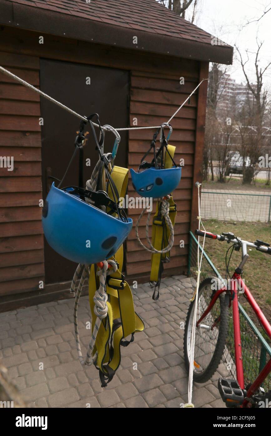 due caschi blu, cinture di sicurezza con moschettoni appendono su una corda sullo sfondo di una casa di legno. Dispositivi di protezione e di protezione per giocare e. Foto Stock