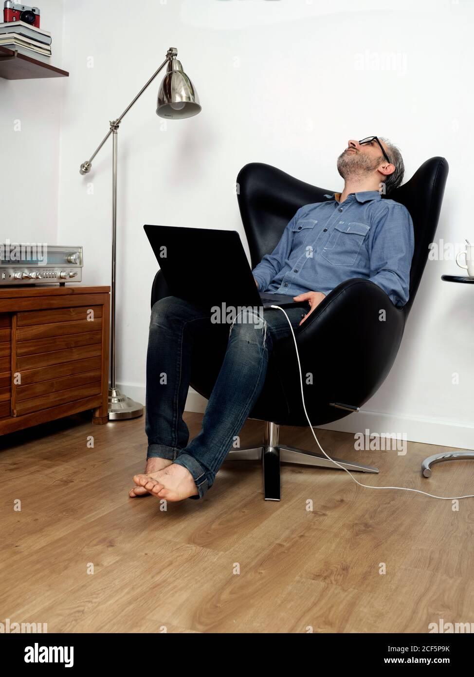 un uomo che lavora su un computer portatile si è sopraffatto sulla poltrona di casa Foto Stock