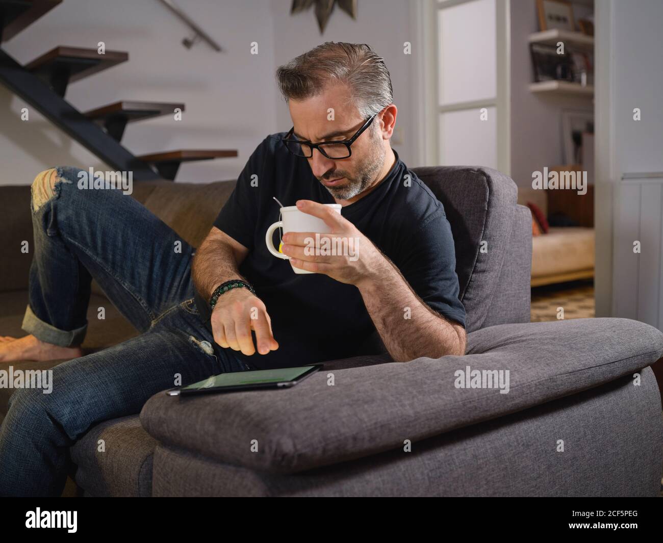 Uomo rilassato navigando su internet con un caffè da solo il divano nel soggiorno di casa Foto Stock