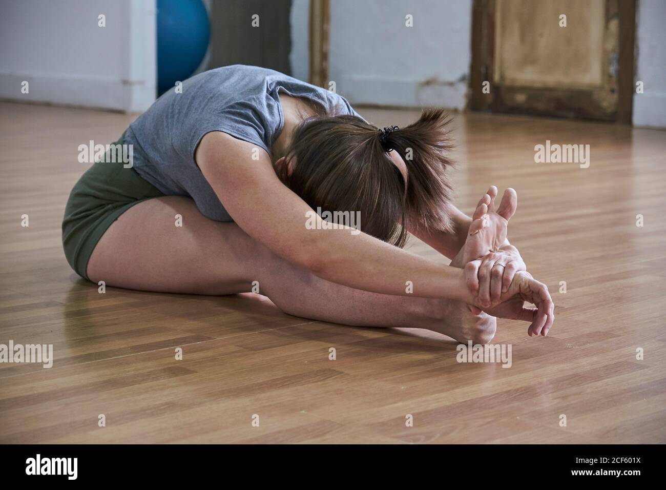 Donna in forma rilassata con occhi chiusi che eseguono la curva seduta in avanti durante l'allenamento yoga in uno spazioso monolocale Foto Stock