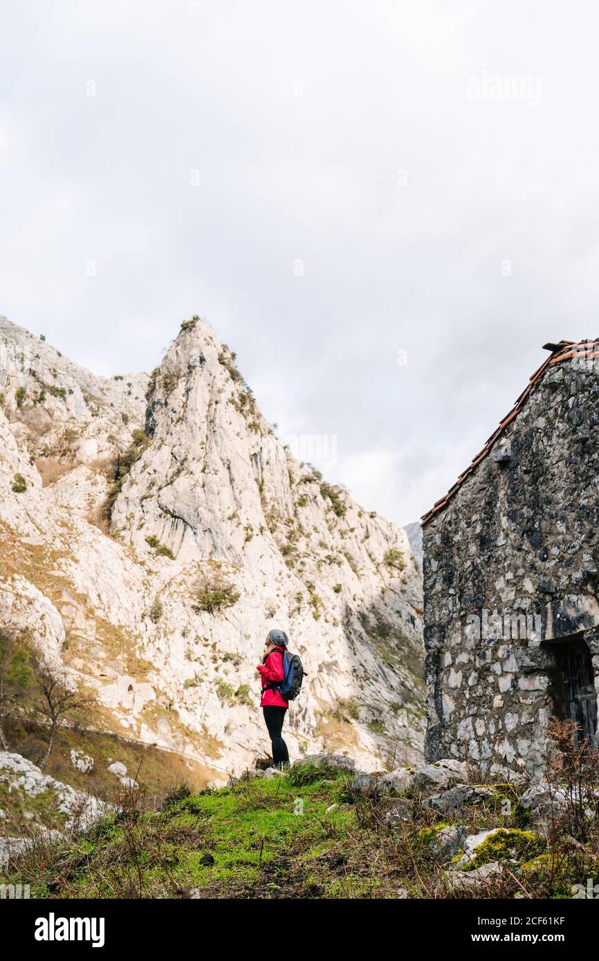 Vista laterale dell'escursionista attivo in giacca rossa con zaino pesante che guarda in cima alla montagna in Europa, Asturie, Spagna Foto Stock