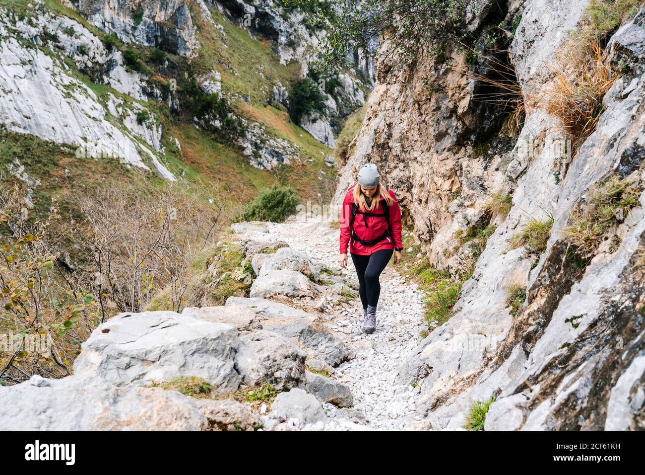 Donna attiva escursionista in giacca rossa con zaino pesante che cammina fino montagna in vette d'Europa, Asturie, Spagna Foto Stock