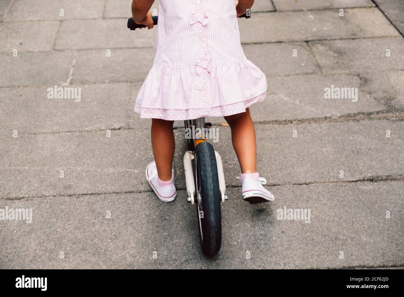 Vista posteriore di bambina irriconoscibile che cavalcano su piccola bici sulla strada Foto Stock