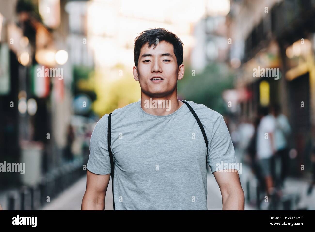 Contenuto moderno giovane etnico uomo in t shirt passeggiando lungo strada urbana estiva Foto Stock