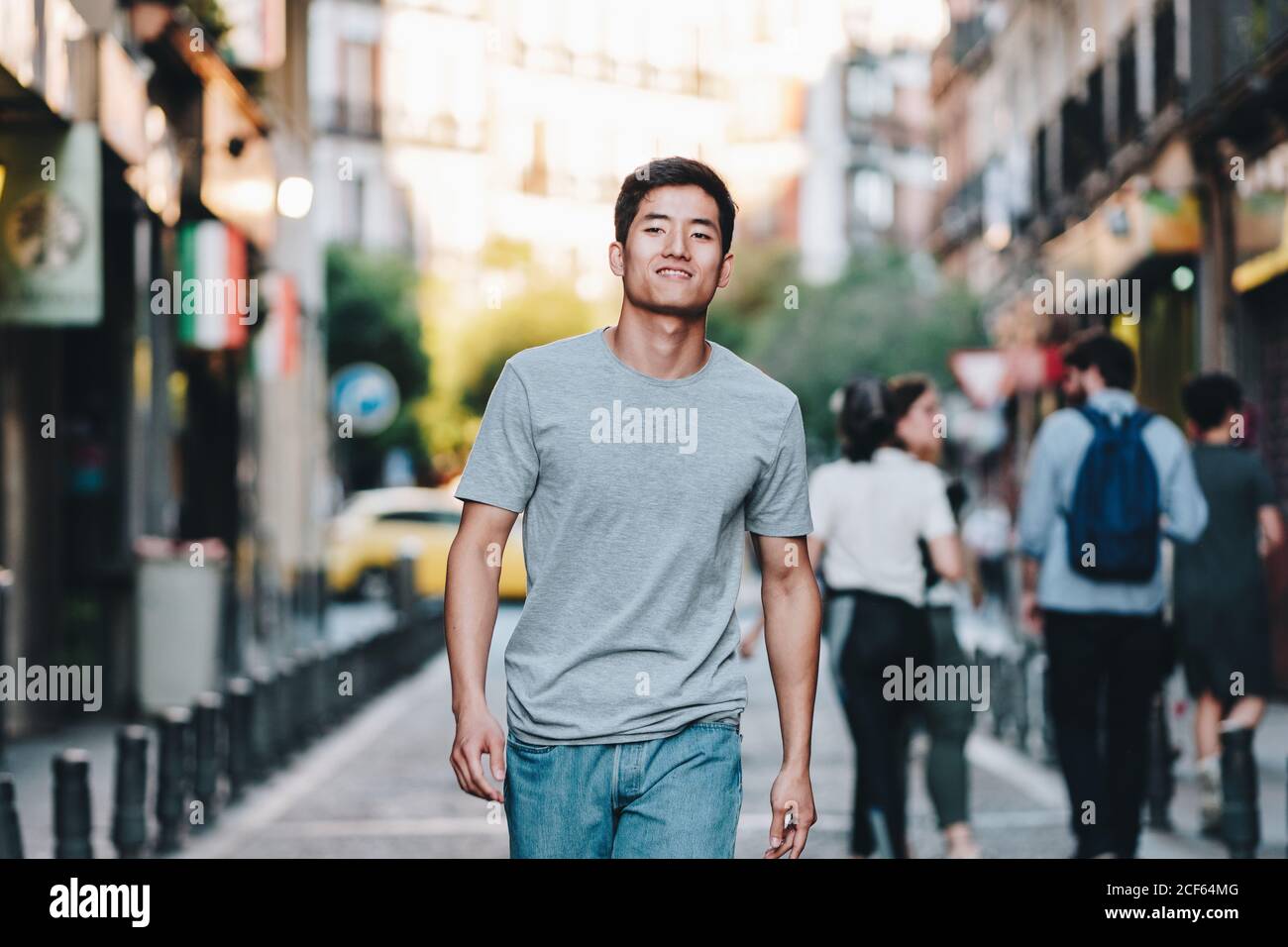 Contenuto moderno giovane etnico uomo in t shirt passeggiando lungo strada urbana estiva Foto Stock