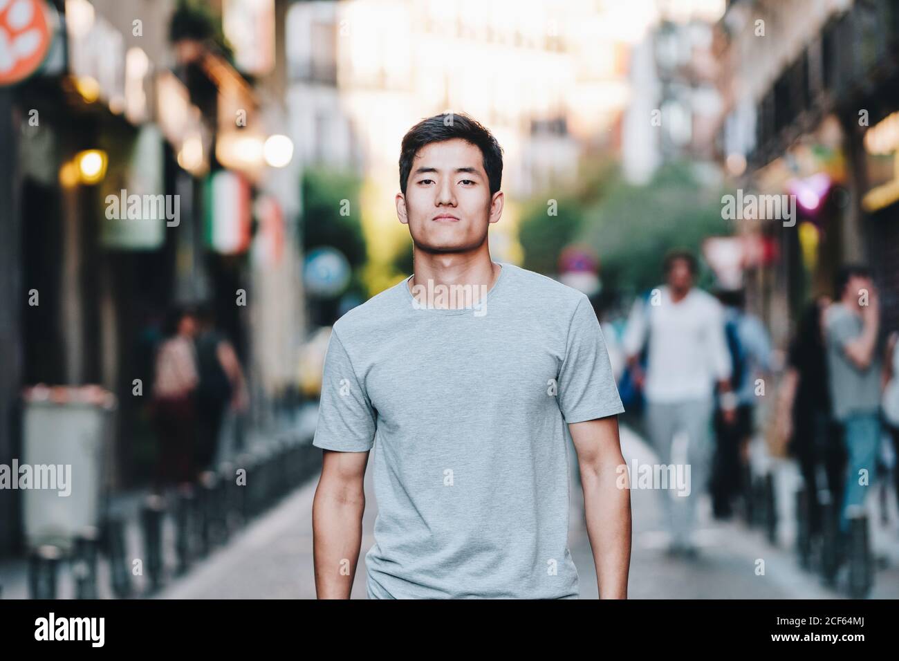 Contenuto moderno giovane etnico uomo in t shirt passeggiando lungo strada urbana estiva Foto Stock