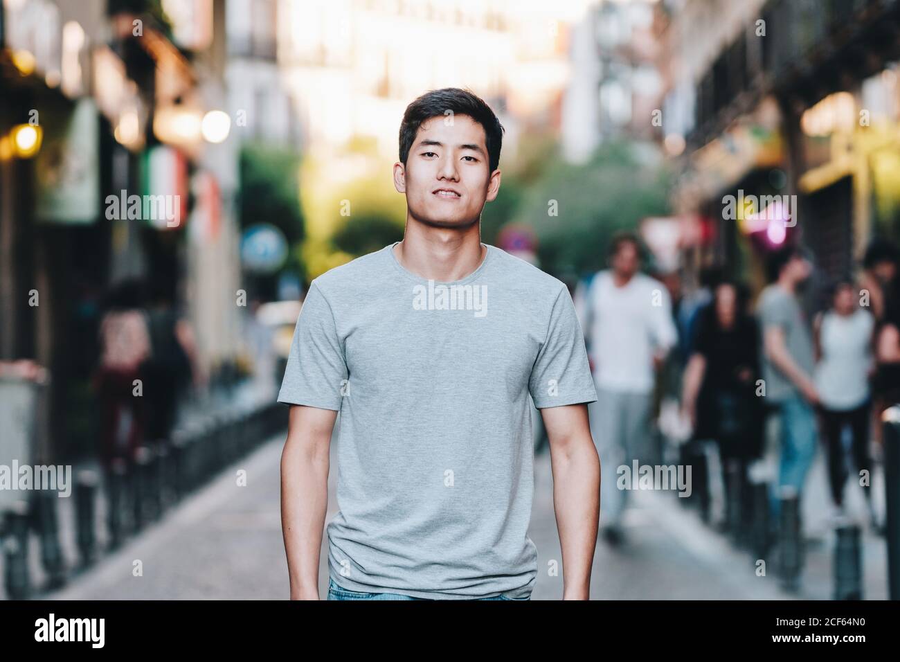 Contenuto moderno giovane etnico uomo in t shirt passeggiando lungo strada urbana estiva Foto Stock