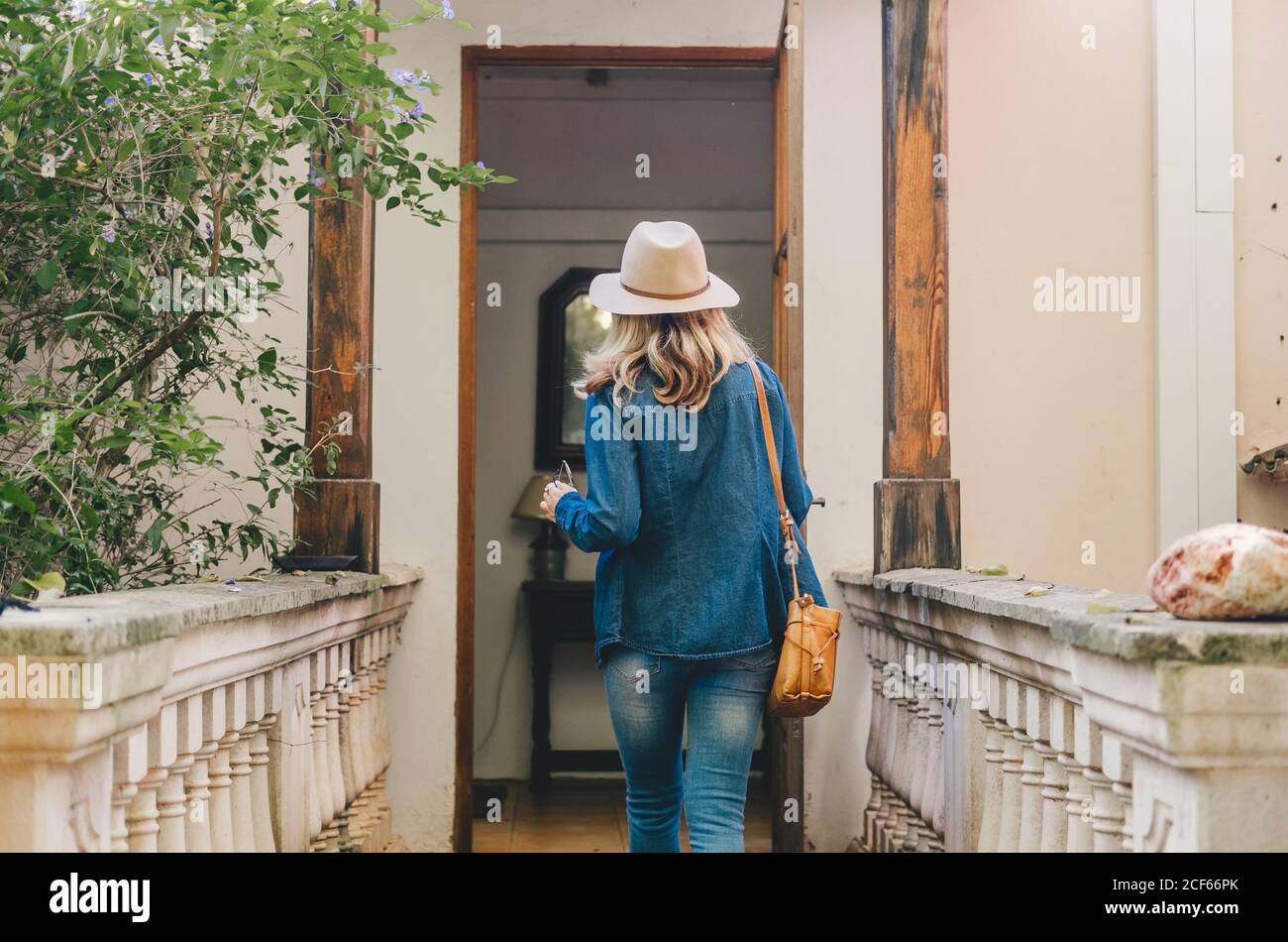 Vista sul retro della giovane donna in denim e cappello che apre una porta in vetro di legno dell'edificio autentico Foto Stock