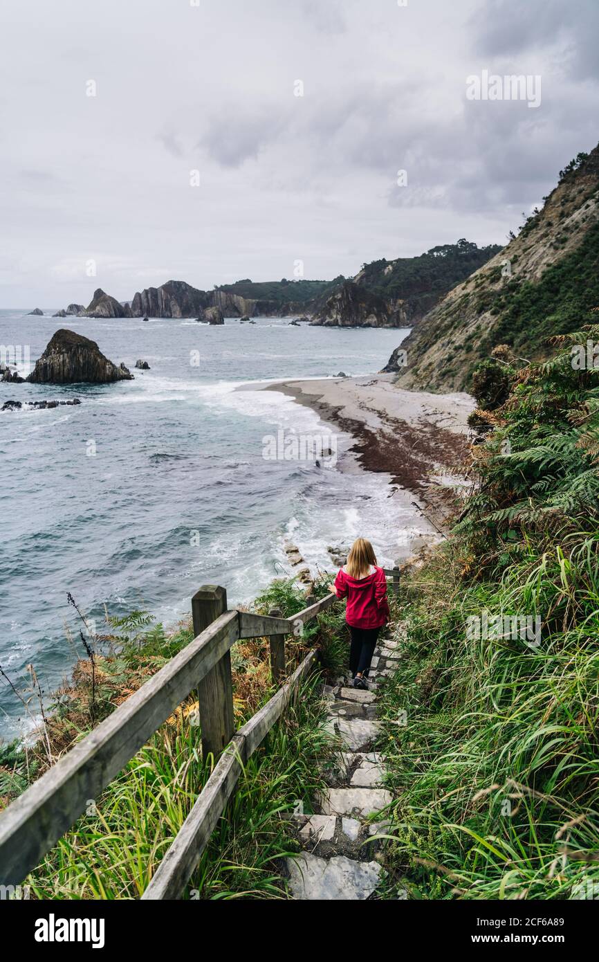 Donna che cammina giù su gradini di pietra che conducono giù a schiumoso mare Foto Stock