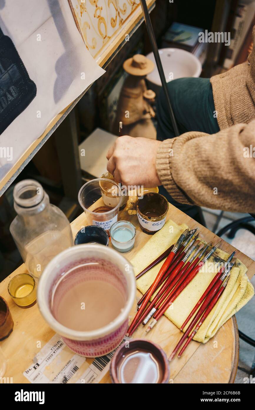 Persona che prende la vernice con la spazzola dal vetro che ha gli attrezzi di disegno intorno Foto Stock