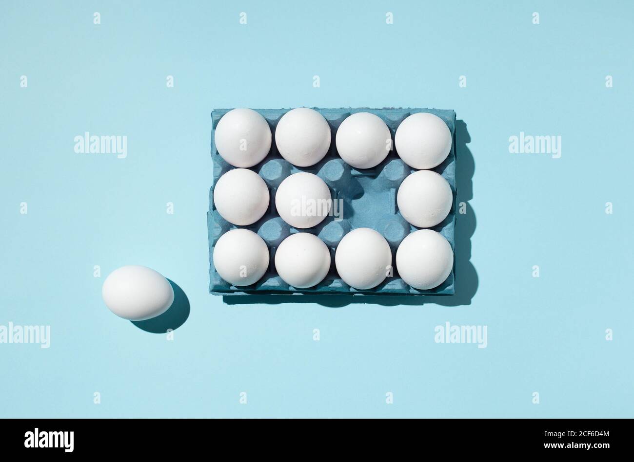 Vista dall'alto delle uova bianche poste nel vassoio di carta che mostra concetto di differenza su sfondo blu in studio Foto Stock