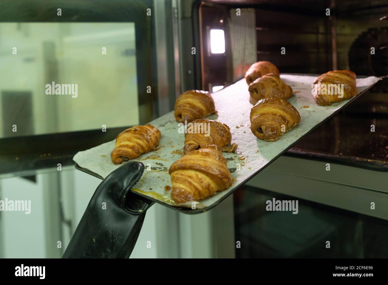 Crop mano in nero guanto da cucina che si estrae dal forno croissant appena sfornati all'interno Foto Stock