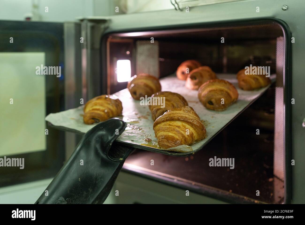 Crop mano in nero guanto da cucina che si estrae dal forno croissant appena sfornati all'interno Foto Stock