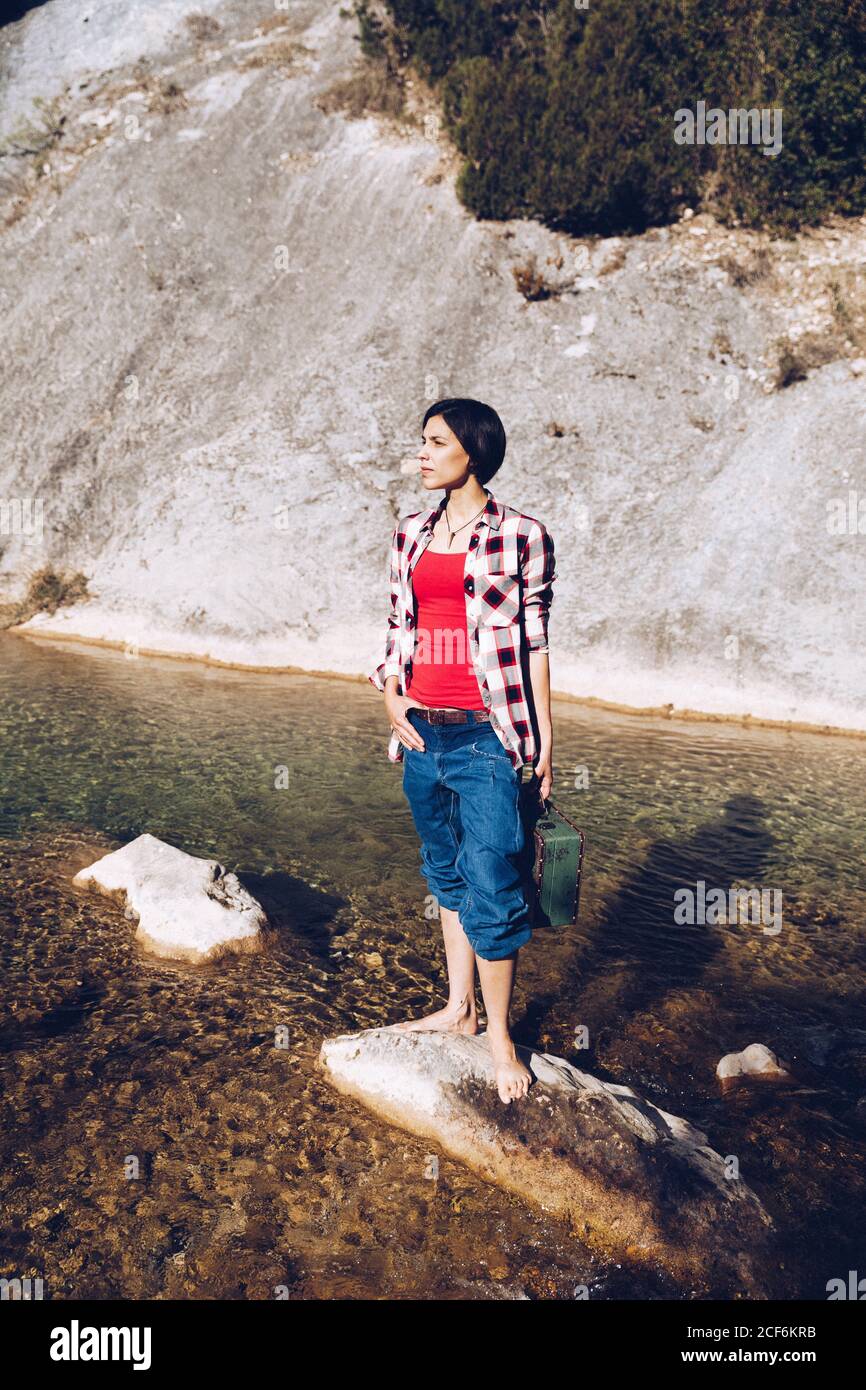 Donna in piedi su roccia con custodia vicino acqua limpida nel lago Foto Stock